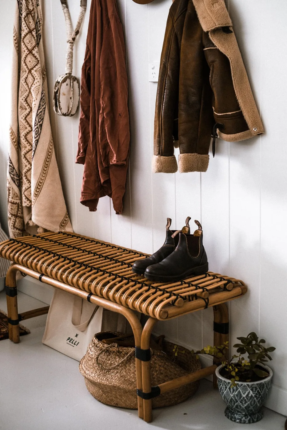 Coats hanging above a woven entryway bench with shoes